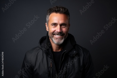 Handsome middle aged man with beard and mustache wearing a black leather jacket on a dark studio background