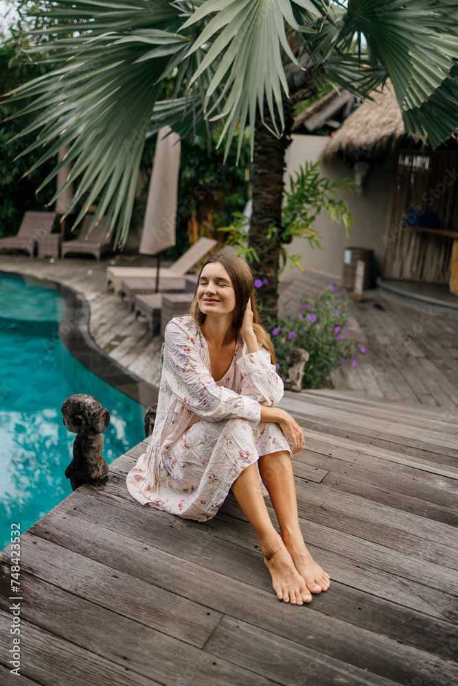 Beautiful caucasian lady in dressi sitting near swimming pool   at tropical summer resort, closed eyes, meditation