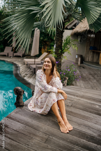 Beautiful caucasian lady in dressi sitting near swimming pool at tropical summer resort, closed eyes, meditation