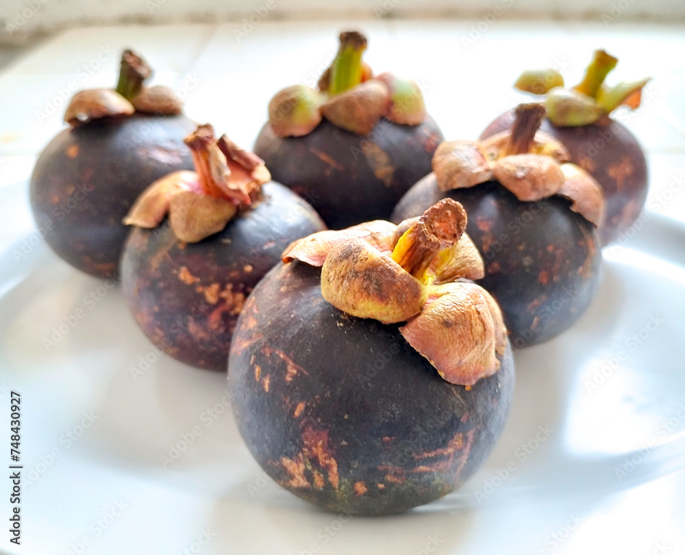 Fototapeta premium Mangosteen (Garcinia mangostana), also known as the purple mangosteen, Clusiaceae family. Group of mangosteen fruit on white plate. Selective focus. 