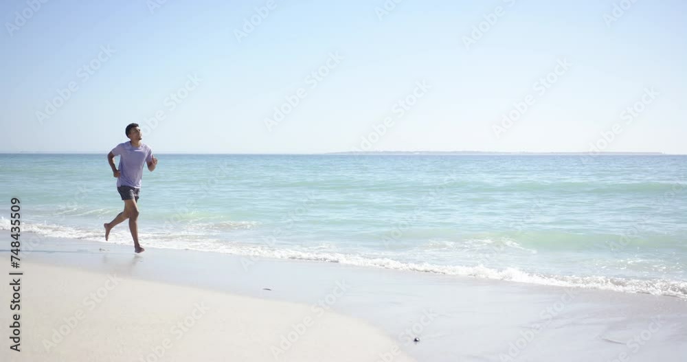 A young biracial man jogs along a sunlit beach with copy space A young biracial man jogs along a sunlit beach with copy space
