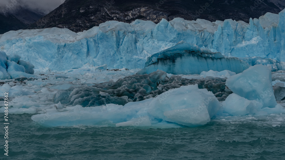 A fragment of a melting glacier. A wall of blue ice with cracks rises in a glacial lake. Melted ice floes float in turquoise water. Close-up. Perito Moreno glacier. El Calafate. Argentina. A fragment of a melting glacier. A wall of blue ice with cracks rises in a glacial lake. Melted ice floes float in turquoise water. Close-up. Perito Moreno glacier. El Calafate. Argentina.