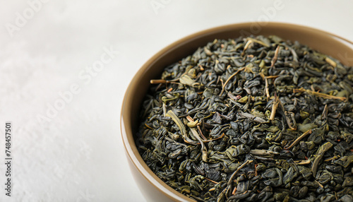 Bowl of dry green tea leaves on light background  closeup view with space for text