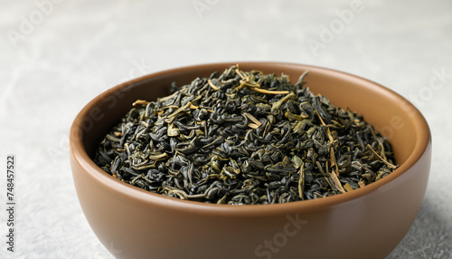Bowl of dry green tea leaves on light background, closeup view with space for text