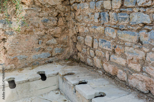 Ruins of an ancient restroom with stone seating in Ephesus, Turkiye