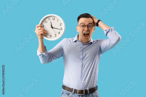 Stressed businessman with clock on blue background. Deadline concept