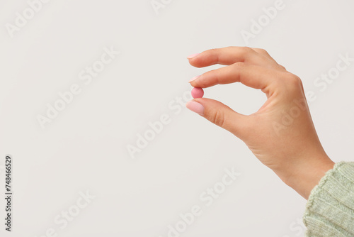 Woman holding pink pill on white background