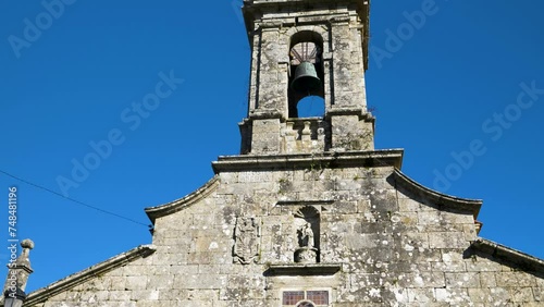 Pan down across old stone bell tower and weathered rocks of San Xoan de Rio church photo