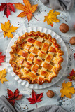 Homemade golden lattice pie on a white plate with autumn leaves and walnuts, perfect for Thanksgiving, with space for text on a rustic table