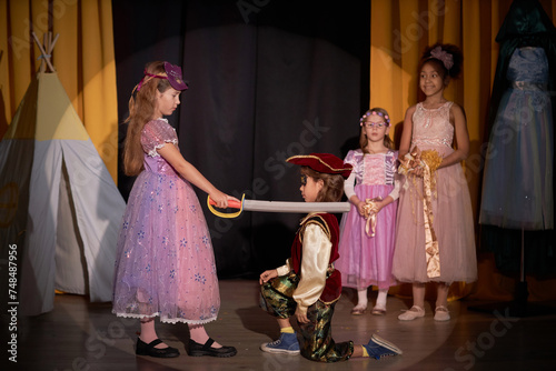 Side view portrait of young girl on stage in school play production acting as warrior princess holding sword and defeating pirate copy space