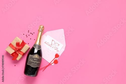 Bottle of champagne with gift box, postcard and decor on pink background. Valentine's Day celebration