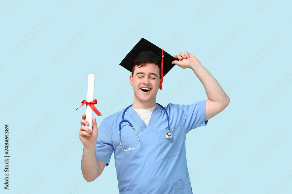 Male student in mortar board and uniform of doctor with diploma on blue background Male student in mortar board and uniform of doctor with diploma on blue background
