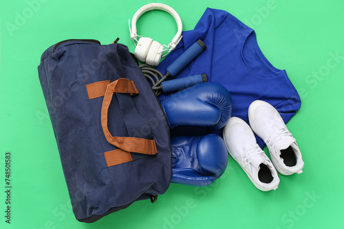 Sports bag with sportswear and boxing equipment on green background
