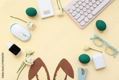 Frame made of Easter eggs, paper, bunny ears, glasses, flowers, computer keyboard and mouse on yellow background