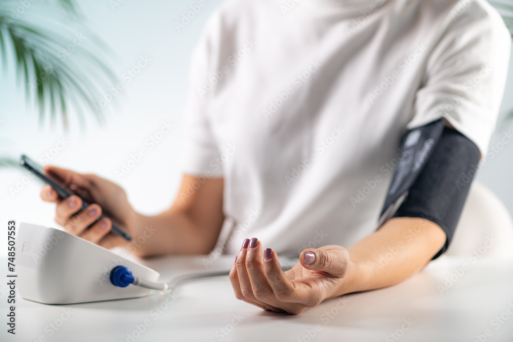 A woman checks her blood pressure at home, focusing on health and well-being - obrazy, fototapety, plakaty 