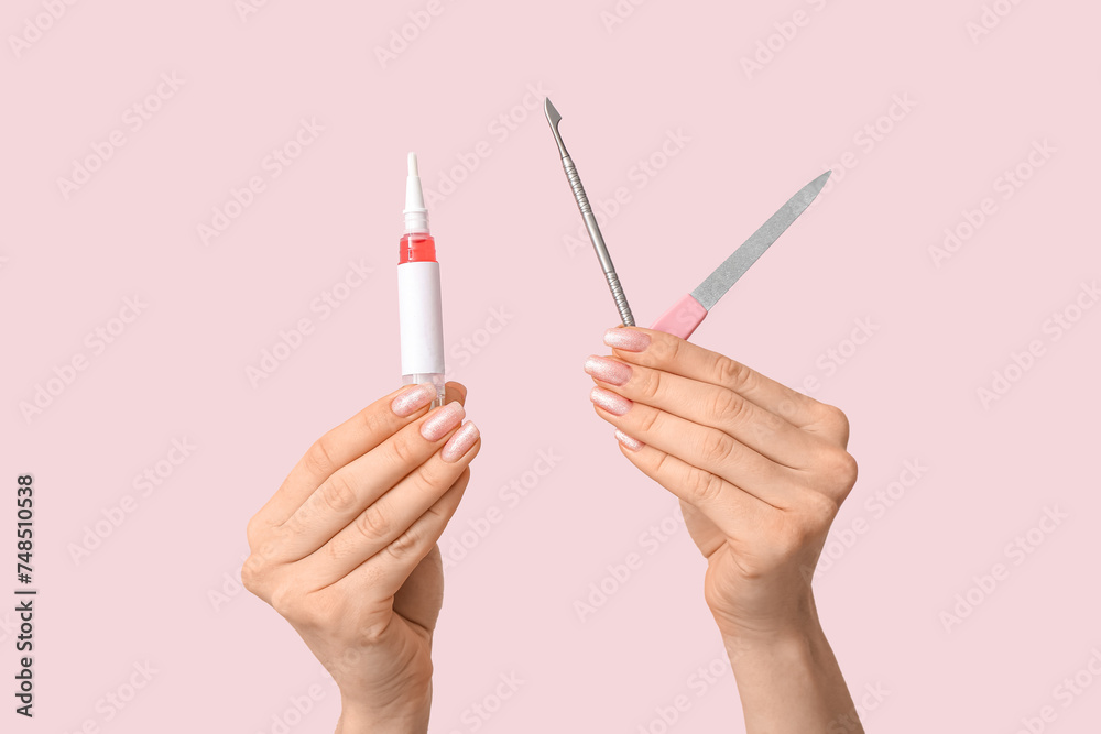 Female hands with cuticle oil pen, pusher and nail file on pink background - obrazy, fototapety, plakaty 