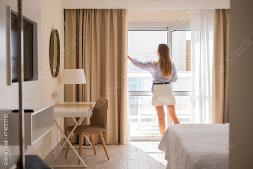 Mujer joven abriendo la ventana corredera de su habitación por la mañana  photo