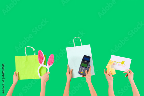 Women with payment terminal, Easter decor and bags on green background. Online shopping