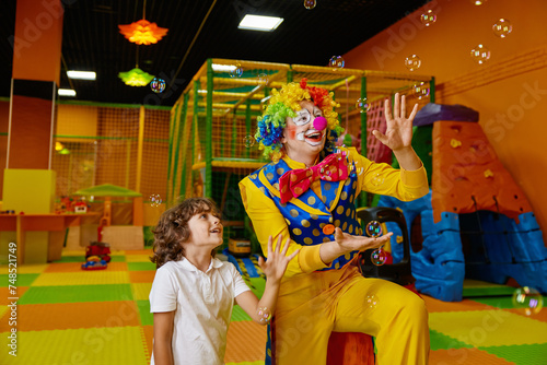 Little preschool boy and clown playing with soap bubbles