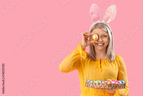 Beautiful woman in bunny ears with Easter eggs on pink background