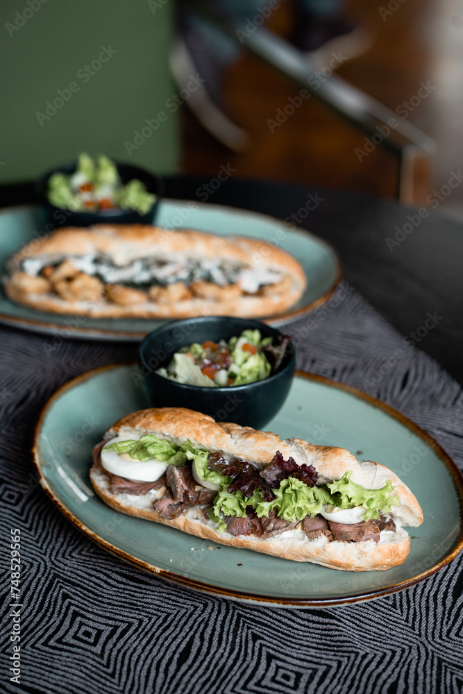 A high angle of two sandwich with meat, eggs, vegetables, and sliced red onion on green plate