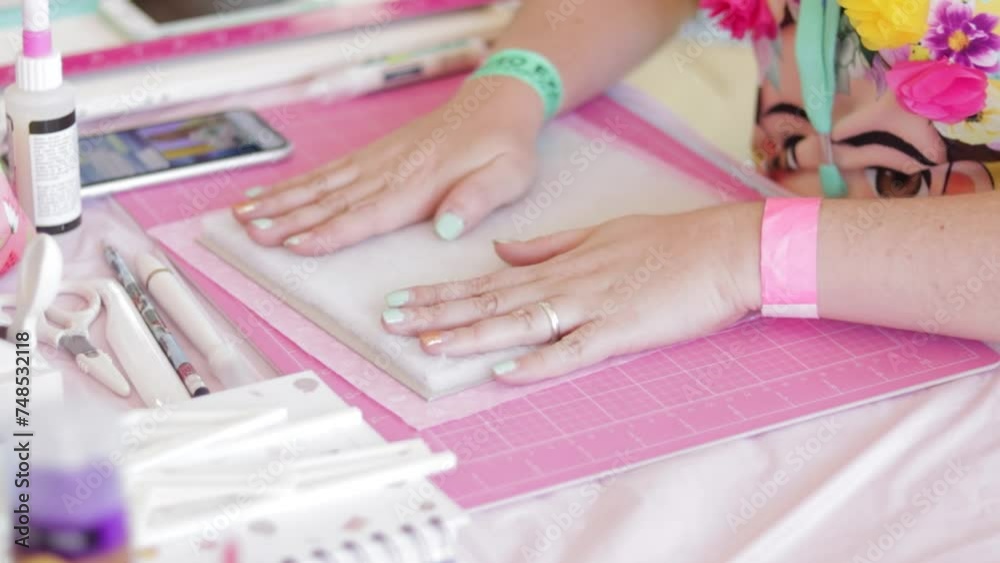 Hands creating a scrapbook on pink mat with crafting tools around, bright colors Hands creating a scrapbook on pink mat with crafting tools around, bright colors