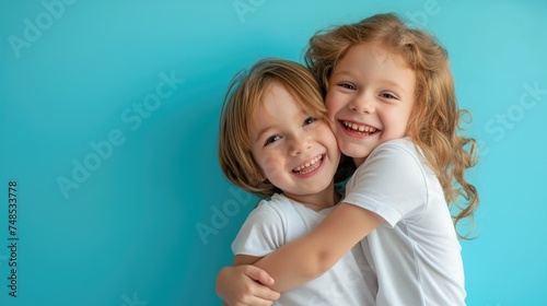 Cute little boy and girl in white t-shirts hugging on blue background. Happy siblings day
