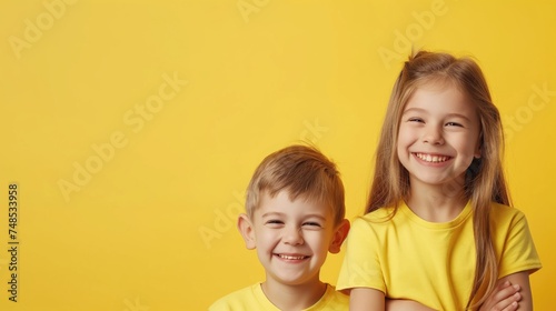 Portrait of two little kids boy and girl in yellow shirts on yellow background. Happy siblings day