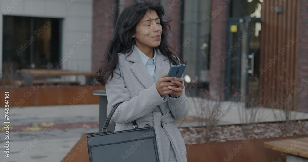 Slow motion of good-looking Middle Eastern lady standing in city street using smartphone touching screen on windy day. Wireless communication and social media concept. Slow motion of good-looking Middle Eastern lady standing in city street using smartphone touching screen on windy day. Wireless communication and social media concept.
