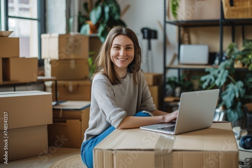 Young female entrepreneur smiling at laptop in a home office with moving boxes