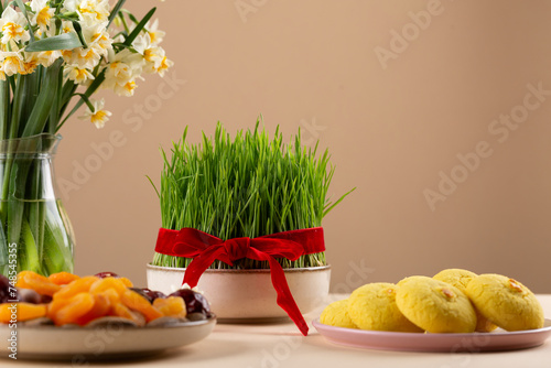 Novruz table setting with green samani wheat grass with red ribbon, dried fruits, sweet pastry, candles, kelagai and blooming flowers, spring or new year celebration in Azerbaijan, copy space