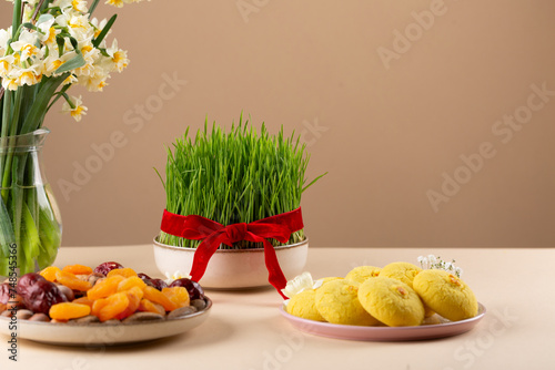 Novruz table setting with green samani wheat grass with red ribbon, dried fruits, sweet pastry, candles, kelagai and blooming flowers, spring or new year celebration in Azerbaijan, copy space
