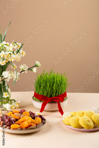Novruz table setting with green samani wheat grass with red ribbon, dried fruits, sweet pastry, candles, kelagai and blooming flowers, spring or new year celebration in Azerbaijan, copy space