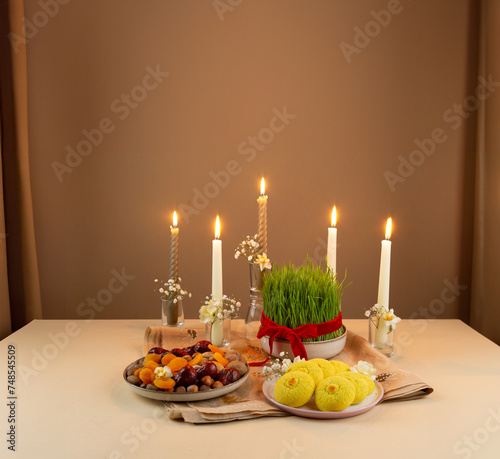 Beautiful Novruz setting on peachy neutral background with fresh semeni wheat glass with red ribbon, candles and traditional Azerbaijani pastry on the table, dried fruits and eggs and daffodils