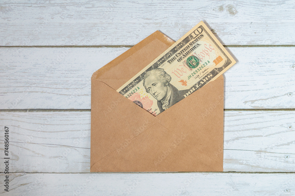 A paper envelope with 10 dollars in it on a white wooden background. Flatley with a gift