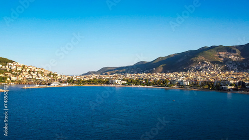 A drone's-eye view captures the stunning panorama of Alanya, where the city meets the beach against the backdrop of majestic mountains, offering a breathtaking tableau of natural and urban beauty