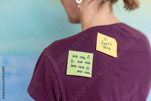 Beautiful young woman with paper stickers attached to her friend's back. April fools day celebration photo