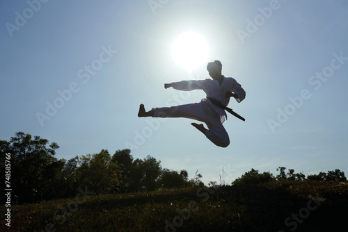 Silhouette of taekwondo athlete doing jump kick in rays on setting sun