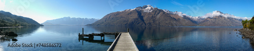 Panoramic view of wooden pier jutting into placid and crystal clear Lake Wakatipu towards Cecil Peak in the Southern Alps on New Zealand's South Island