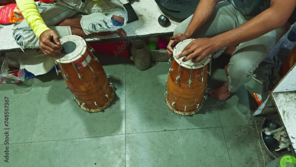 Two people sitting and playing traditional Indian tabla drums with focus on hands and instruments man repairing drum at musical workshop