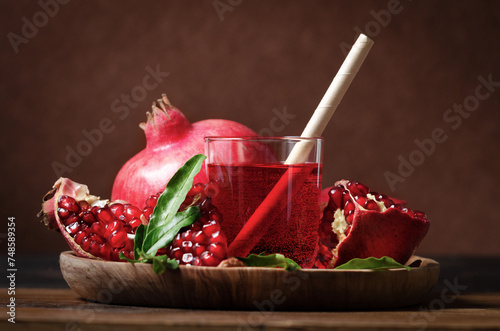 Fresh juice of pomegranate with fruit and leaves on wooden plate on dark rustick background.