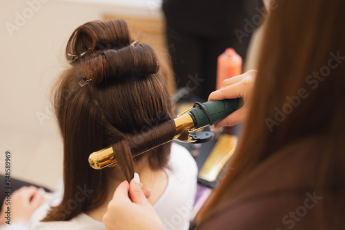 Portrait happy woman hairdresser stylist skillfully curling hair with golden iron in salon, hairstyle for wedding