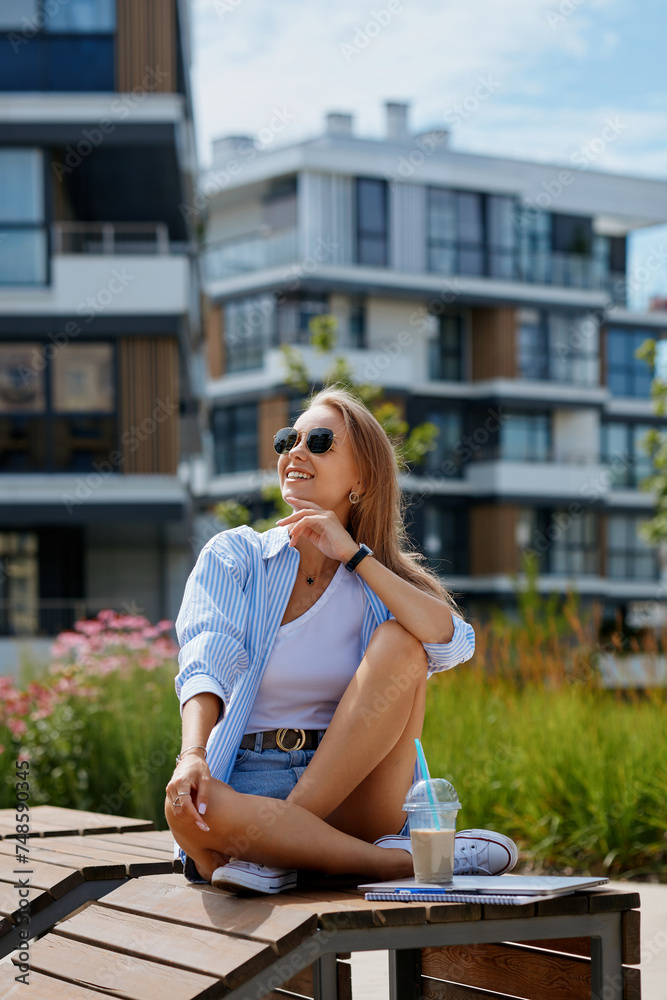 Beautiful young woman dressed in a summer look with sunglasses against the background of a building