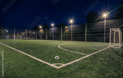 An amateur soccer field with ball illuminated at night. A small football field lit by lanterns in the evening. Green football field illuminated at night. Soccer field in night with spotlight photo