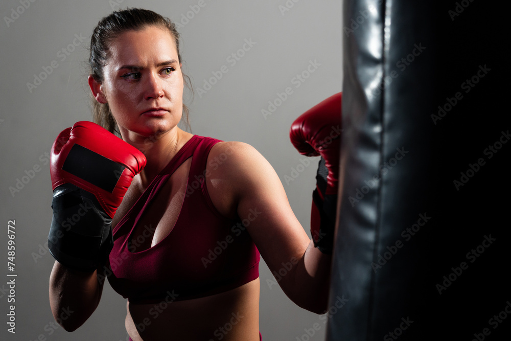 Portrait of a boxer woman in a red tracksuit hitting a punching bag
