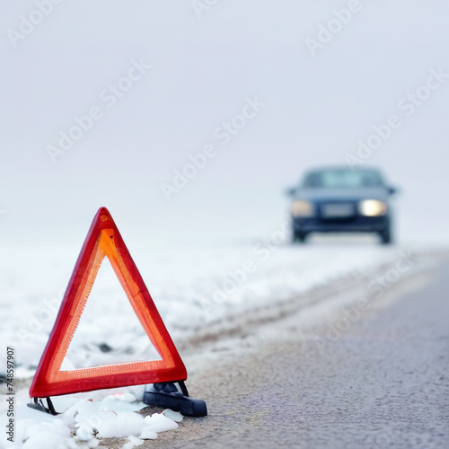 red warning triangle with a car on a snowy  winter road