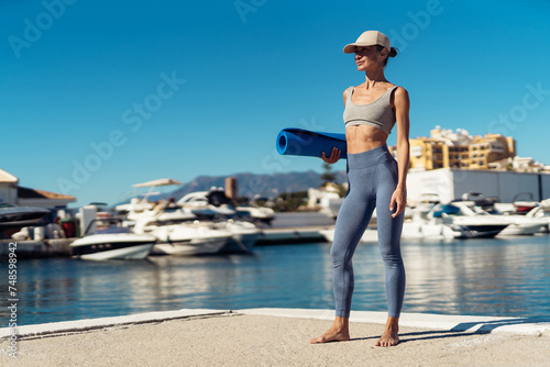 A fitness girl holds a fitness mat in her hands. Girl before training with a fitness mat. Outdoor training. sports motivation. there is space for text