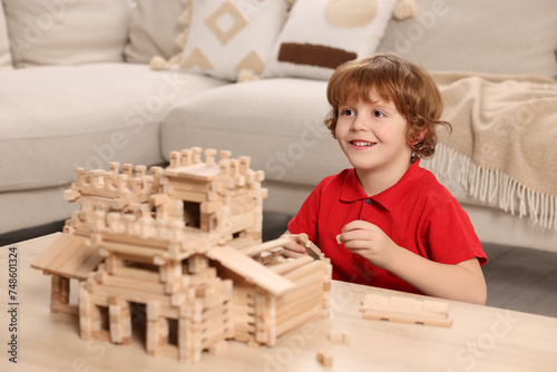 Cute little boy playing with wooden castle at table in room. Child's toy