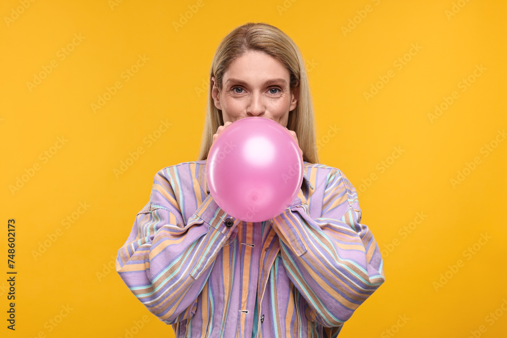 Woman blowing up balloon on yellow background Woman blowing up balloon on yellow background