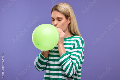 Woman blowing up balloon on violet background © New Africa